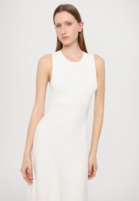 Abito bianco a coste senza maniche con corpetto aderente e gonna fluida, caratterizzato da una texture liscia e un design minimalista.