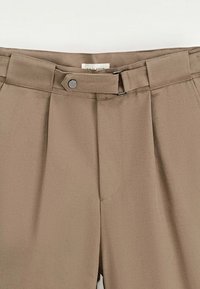 Pantalons beige ajustés avec une texture lisse, dotés d'un devant plissé, d'une fermeture à bouton métallique et d'une taille piquée.