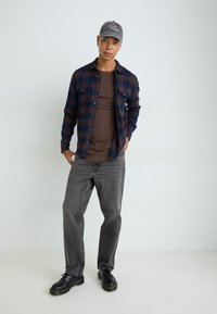 Plaid blue and brown flannel shirt over a brown T-shirt, gray jeans, and black shoes with yellow accents. Embroidered gray cap.