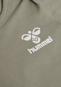 Olivgrön tyg med en slät textur. Vitt logo med en stiliserad bi och texten "hummel" nära halsringningen. Enkelt, rent design.