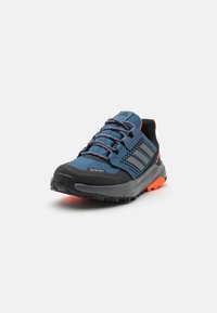 Zapatillas de trail azul y negra con detalles en naranja, parte superior de malla con puntera reforzada, suela texturizada para agarre y cordones flexibles.