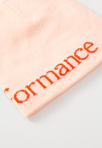 Soft pink fabric folded with bright orange text partially reading "formance" on a plain white background.