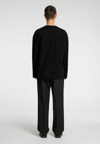 Svart oversized langermet skjorte med rund hals, vist bakfra, kombinert med svarte vidbukser og svarte sko.