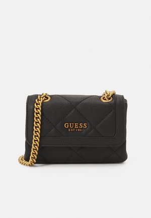 Sac à main GUESS en cuir noir matelassé avec bandoulière chaîne dorée et logo doré "GUESS EST 1981" sur le rabat avant.