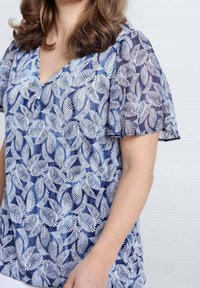 Bloemenblouse in blauw en wit met een V-hals, korte mouwen en een lichtgewicht, semi-transparante stof met bladpatronen.