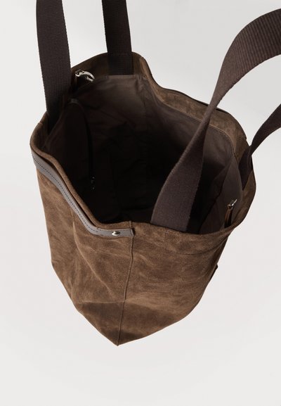Sac cabas en daim marron avec deux poignées en tissu foncé, ouverture en haut et poche intérieure zippée visible à l'intérieur.