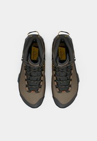 Sapatilhas de caminhada castanhas e pretas com atacadores padrão e puxadores amarelos, vistas de cima sobre um fundo branco.