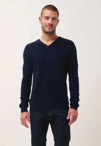 Dunkelblauer Pullover mit langen Ärmeln und V-Ausschnitt sowie gerippten Bündchen. Weicher Stoff, körperbetonte Form und minimale Details.