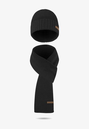 Black knit beanie and scarf set featuring ribbed texture, with a strip of brown leather branding on both pieces. Soft, warm material.