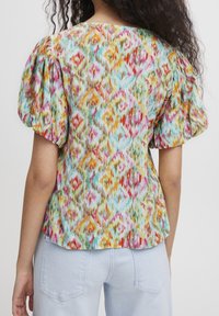 Blouse à motifs multicolores avec manches bouffantes, présentant un design vibrant dans des tons de rose, orange et bleu sur un fond clair.