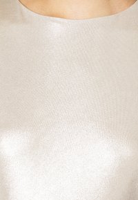 Detailní záběr osoby v lesklém, hladkém stříbrném nebo metalické béžovém vysokém oděvu.