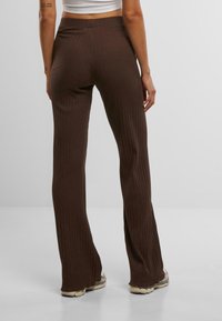 Pantalons marron à côtes évasés avec une taille haute, fabriqués dans un tissu texturé et adaptés au niveau des cuisses, s'élargissant vers le bas.