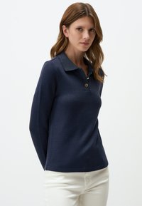 Navy blauw polo shirt met lange mouwen, een gestructureerde oppervlakte, knopenlijst en contrasterende kraag. Gestyled met lichtgekleurde broek.