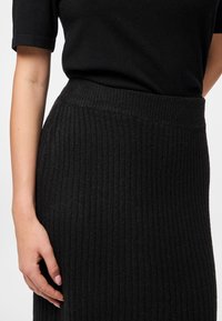 Črna rebrasta pletena krila s širokim pasom, ki ima strukturo navpičnega vzorca. Tkanina izgleda mehka in nekoliko elastična.