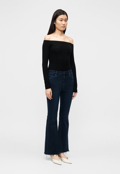 Must off-the-shoulder pikkade varrukatega topp, mille juurde on kombineeritud tumesinised lõdvalt hõlmavad teksad, millel on töötlemata ääred ja istuv vöökoht. Kandmisel heledavärvilised kontsakingad.