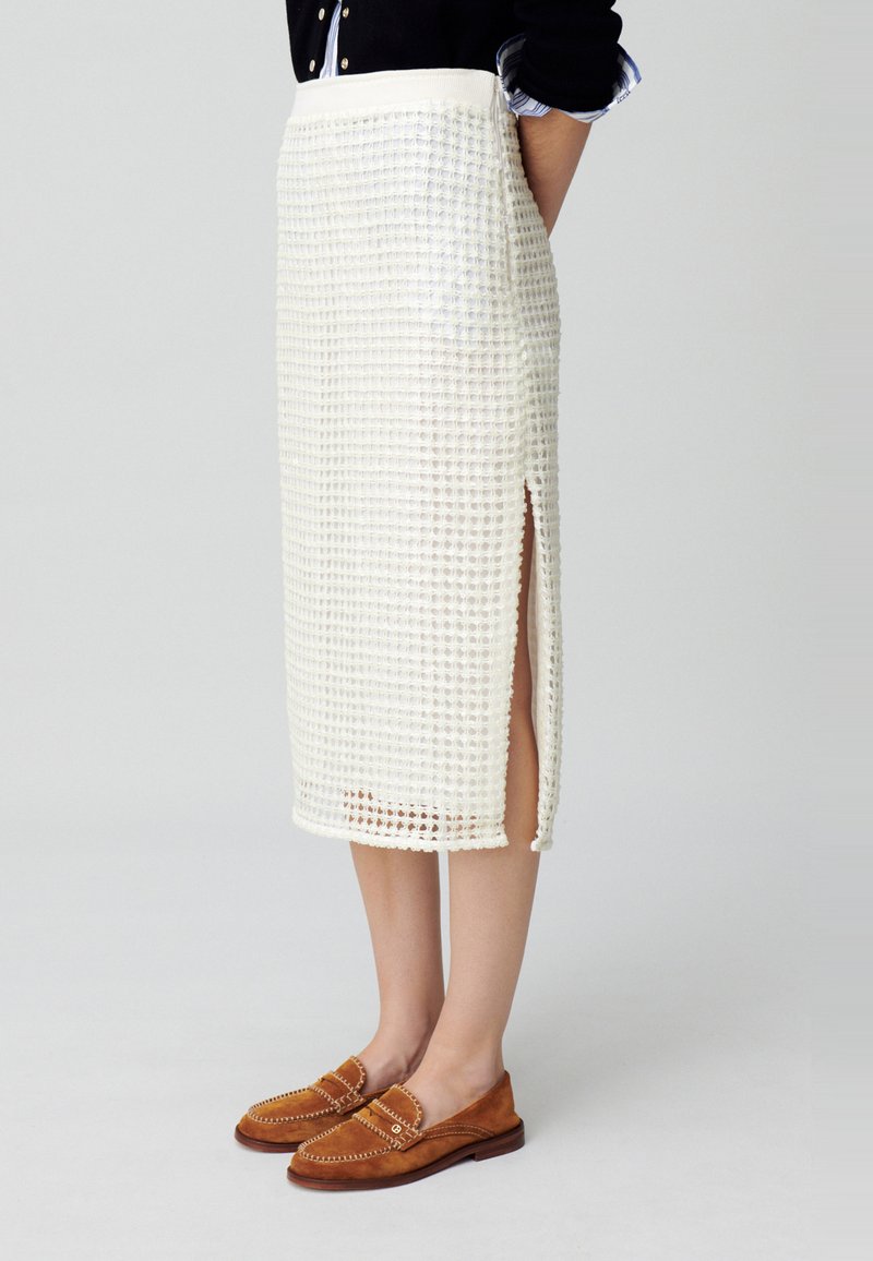 Jupe midi en crochet blanc avec surface texturée et fente sur le côté, associée à des mocassins en suède marron avec des accents en couture.