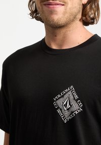 Czarny bawełniany t-shirt z geometrycznym białym logo graficznym umieszczonym na środku klatki piersiowej, z ostrym kołnierzykiem i krótkimi rękawami.