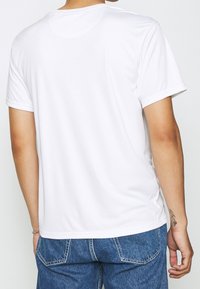 Camiseta blanca de manga corta con cuello redondo. Textura suave, diseño sencillo y sin patrones ni acentos visibles.