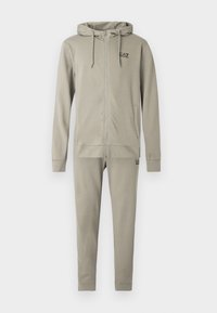 Világosszürke kapucnis cipzáras pulóver és hozzá illő melegítőnadrág kis EA7 Emporio Armani logókkal a mellkason és a combon.