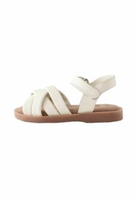 Vita läder sandal med korsade remmar, justerbar vristrem och en tan-texturerad sula. Minimalistisk design för komfort.