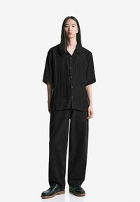 Maglietta nera a maniche corte con un design a coste texturizzate, abbinata a pantaloni neri a gamba larga e scarpe nere con suola spessa.