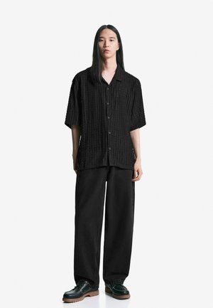 Zwarte korte mouw shirt met een gestructureerd ribfluwelen ontwerp, gecombineerd met zwarte wijde broek en zwarte schoenen met een dikke zool.