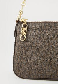 Brązowa torebka crossbody w wzór z złotymi elementami i zapięciem na zamek. Posiada płaską formę, z teksturowanym wykończeniem i detalem z logo. Regulowany łańcuszek na ramię.