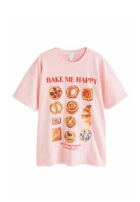 Różowa bawełniana koszulka z krótkim rękawem, z grafiką ciast i tekstem „BAKE ME HAPPY” oraz „PASTRY OVER PROBLEMS” w kolorze czerwonym. Luźny krój.