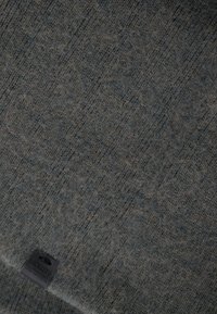 Strukturierter grauer Stoff mit einem subtilen Muster. Enthält ein schwarzes Etikett mit geprägtem Text. Weiches Material mit leicht flauschiger Optik.