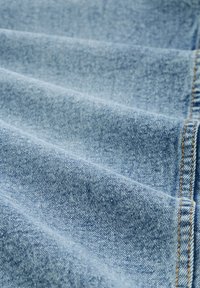 Tessuto di denim azzurro chiaro con un motivo a spina di pesce, caratterizzato da una texture sottile e cuciture gialle visibili lungo i bordi.