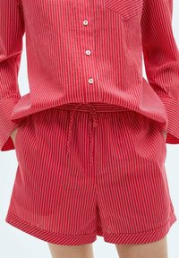 Ensemble de pyjama à rayures rouges comprenant une chemise à boutons avec des manches longues et une poche, associé à un short à taille élastique. Tissu doux et respirant.