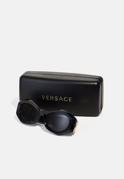 Svart Versace-solbriller har en karakteristisk åttkantet ramme og mørke linser, sammen med et slankt svart etui med gulllogo-detaljer.
