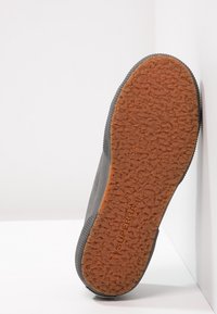 Grå sneakers med en texturerad gummisula, som har en mönstrad yta och en stabil, förstärkt häl. Varumärkesnamn synligt på sulan.