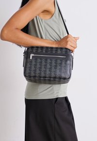 Borsa a tracolla nera a motivi geometrici con chiusura a zip, realizzata in materiale liscio, dotata di tracolla staccabile e dettagli del logo discreti.