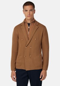 Blazer marrón de doble botonadura con un patrón de punto texturizado, que cuenta con dos bolsillos frontales y un cuello con cremallera. Un ajuste moderno y ajustado.