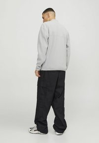 Giacca in pile grigia chiara con colletto alto, abbinata a pantaloni cargo neri larghi con tasche laterali e vestibilità rilassata. Sneakers bianche completano l'outfit.