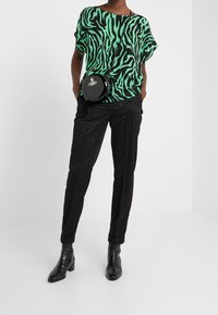 Grön och svart zebramönstrad kortärmad topp, svarta slim-fit byxor och svarta ankelboots. Rund svart axelremsväska med logotyp.