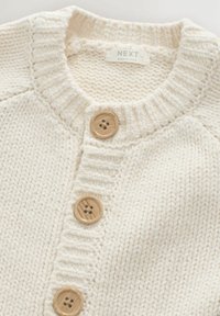 Cremfarbener gestrickter Cardigan mit einem gerippten Kragen und drei Holzknöpfen auf der Vorderseite, der mit einem strukturierten Garn versehen ist.