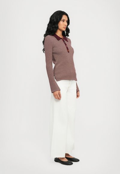 Long-sleeve, fitted maroon ribbed polo with a maroon collar and three buttons. Paired with wide, white trousers and black flats.