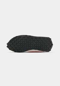 Black rubber outsole with a textured pattern, featuring small raised studs and a smooth area. Accented with a light beige and red upper edge.