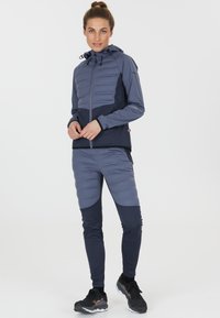 Vadderad marinblå och mörkblå huva-jacka med dragkedja fram, tillsammans med åtsittande marinblå byxor med en texturerad design och kontrasterande detaljer.