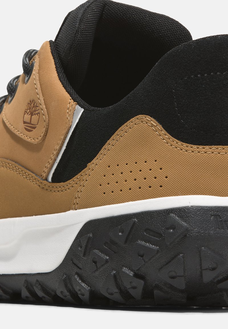 Bruine en zwarte sneaker met een gestructureerde bovenkant, geperforeerde details en een witte tussenzool. Voorzien van een rubberen outsole met tractiepatronen.