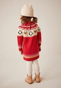 Vestito rosso lavorato a maglia con giromanica a fantasia che presenta pinguini e renne, polsini e orlo a costine. Abbinato a un berretto lavorato a maglia beige e stivali beige.
