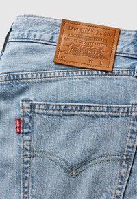 Lyseblå denimjeans med en brun lærplakett i midjen. Har oransje søm og en rød Levi's-lapp på baklommen.