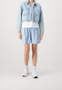 Světlá modrá krátká džínová bunda, bílé tričko a modré pruhované šortky. Bílé tenisky s černými podrážkami. Ležérní střih a uvolněný design.