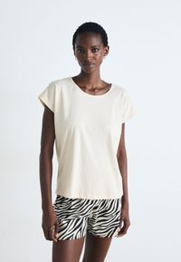 Kortärmad, krämfärgad bomullströja med rund halsringning, kombinerad med svarta och krämfärgade zebra-mönstrade shorts. Slen textur, avslappnad passform.