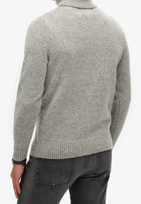 Grijze gebreide coltrui met geribbelde manchetten en zoom, gemaakt van gestructureerd garen, met een aansluitende pasvorm, gedragen over donkere spijkerbroek.