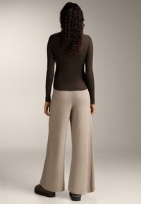 Braun geripptes Langarmoberteil kombiniert mit beigen weit geschnittenen Strickhosen und dunklen Schuhen. Einfaches, strukturiertes Design und lässige Passform.