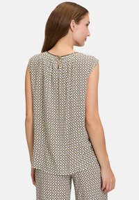 Kortärmad, mönstrad blus i beige och vitt med geometrisk design. Har en nyckelhål-stängning bak och är i mjukt, lätt tyg.