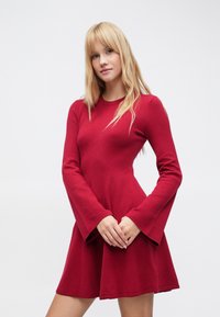 Piros hosszú ujjú ruha, testhezálló felsőrésszel és bővülő ujjakkal, puha anyagból készült. A szoknya deréktól tágul, így áramlást kölcsönöz a ruhának.